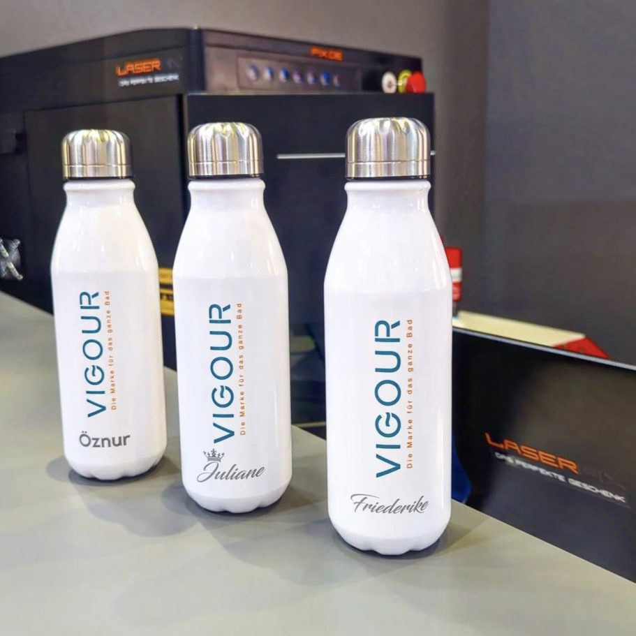 Messe laserarbeit Drei weiße Trinkflaschen mit dem Schriftzug "VIGOUR" auf einem Tisch.