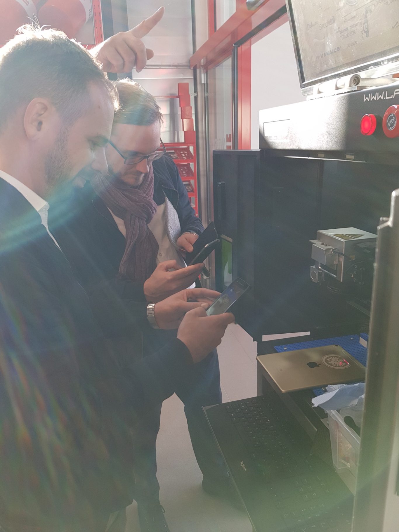 Drei Personen in einem Raum, die Smartphones nutzen und Gerätschaften inspizieren.