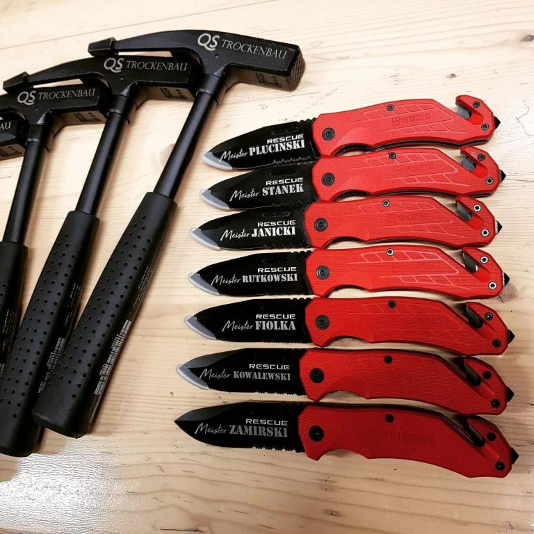 Gravur vor Ort von LASERPIX WÜRTH Zwei schwarze Hämmer und eine Reihe roter Klappmesser auf einem Holzuntergrund.